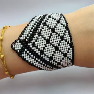 May include: A black and white beaded bracelet with a geometric pattern. The bracelet is made of small, round beads that are woven together to create a unique design.