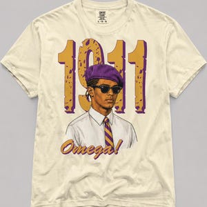 Puede incluir: Una camiseta de color crema con el gráfico de una persona que lleva una boina morada, gafas de sol negras, una camisa blanca de cuello y una corbata a rayas moradas y doradas. El texto 1911 y Omega! aparecen en letras grandes.