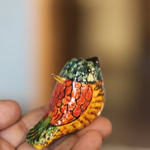 May include: A colorful, hand-painted bird figurine made of paper mache. The bird is painted in shades of blue, green, yellow, orange, and red. It has a small beak and a round body.