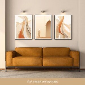 Puede incluir: Tres impresiones de arte abstracto en tonos beige y naranja. Las impresiones est&aacute;n enmarcadas en negro y colgadas en una pared blanca sobre un sof&aacute; de cuero marr&oacute;n.