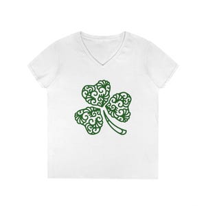 Puede incluir: Camiseta blanca con cuello en V con un diseño de trébol verde. El trébol tiene un patrón detallado y arremolinado. La camiseta es de estilo casual, adecuada para el Día de San Patricio o para uso diario.
