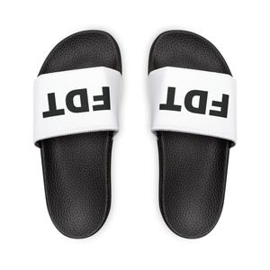 May include: Pair of black and white slide sandals. The sandals have a black textured sole and a white strap with the letters "FDT" printed in bold black font. The sandals are viewed from above.