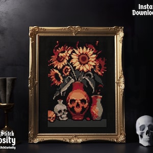 以下が含まれることがあります： ひまわり、頭蓋骨、その他の装飾品が入った花瓶を描いたクロスステッチパターン。パターンは金色の額縁に収められ、暗い背景に飾られています。