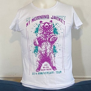 May include: White t-shirt with a purple bear graphic and the text "My Morning Jacket 2023 New York Beacon Theatre 20th Anniversary Tour".