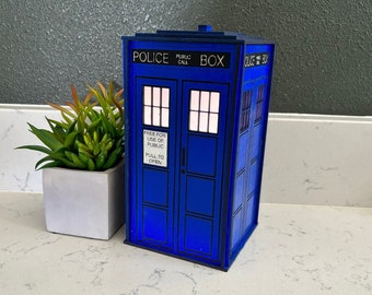 May include: A blue and black police box with a sign that reads "Free for use of public, pull to open". The box has a public call box sign on the top.