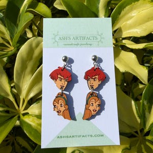 Puede incluir: Pendientes colgantes de madera con caras de personajes de dibujos animados. Los pendientes tienen un perno plateado y un personaje masculino pelirrojo sobre un personaje femenino de pelo largo con una diadema verde. El texto "ASH'S ARTIFACTS" y "ashsartifacts.com" es visible.