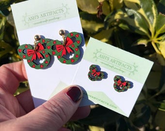 May include: Wooden earrings shaped like a mouse head, featuring a green wreath and a red bow. The earrings are displayed on a white card with the text "Ash's Artifacts - woodcraft jewellery".