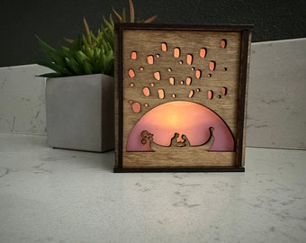 May include: A wooden box with a light inside, depicting a couple in a gondola with lanterns floating above them. The box is lit from within, casting a warm glow.