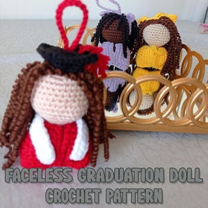 May include: A crocheted graduation doll with a red gown and a black graduation cap. The doll has brown hair and a white face. The doll is sitting on a gold tray with other crocheted dolls.
