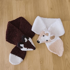 Può includere: Due sciarpe fatte a mano a tema animale. Una è una sciarpa a volpe bordeaux scuro con dettagli bianchi e neri. L'altra è una sciarpa a pecora bianca e beige con una consistenza soffice.