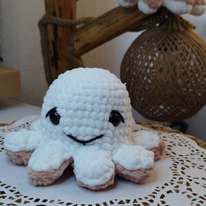May include: A white crocheted octopus with pink accents and black eyes sits on a white doily on a woven basket.