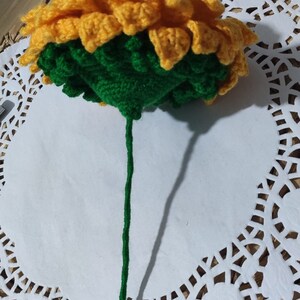 K&ouml;nnte beinhalten: Eine geh&auml;kelte Sonnenblume mit gelben Bl&uuml;tenbl&auml;ttern und einer gr&uuml;nen Mitte, die an einem gr&uuml;nen Stiel befestigt ist.