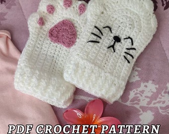 May include: A crochet pattern for a pair of white cat paw mittens. The mittens have pink paw pads and black embroidered cat faces. The pattern is available as a PDF download.