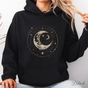 Op de afbeelding: Zwarte hoodie met een gouden halve maan en sterrenprint. De maan is omringd door een cirkel van sterren.