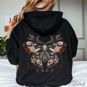 May include: Black hoodie with a large, detailed graphic of a moth with red, white, and black accents. The moth is surrounded by floral elements.