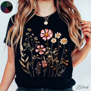 May include: Black t-shirt with a floral print featuring pink and gold pressed flowers. The flowers are arranged in a bouquet-like design.