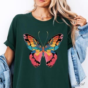 Pu&ograve; includere: T-shirt verde scuro con una grande grafica a farfalla colorata. Il design della farfalla incorpora sfumature di arancione, rosa, giallo e blu. La maglietta ha maniche arrotolate e una vestibilit&agrave; casual.