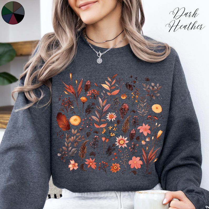 May include: A dark heather grey sweatshirt with a floral print featuring orange, brown, and white flowers and leaves. The text "Dark Heather" is visible in the top right corner of the image.