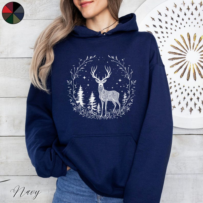 May include: Navy blue hoodie featuring a white illustration of a deer with antlers, surrounded by a wreath of leaves, trees, and stars. The word "Navy" is written in cursive at the bottom left.