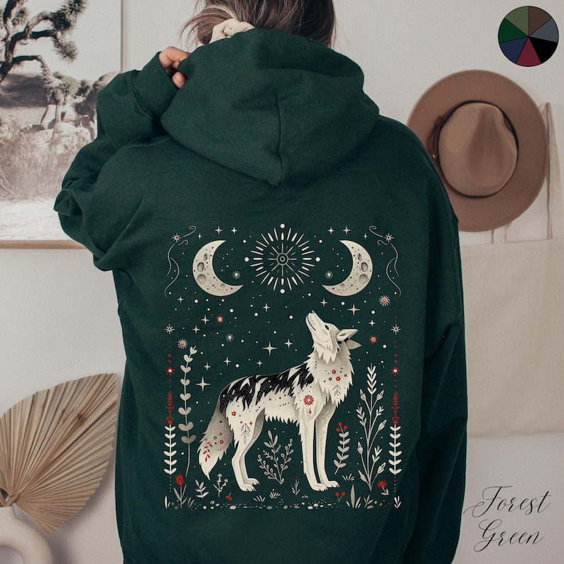May include: Forest green hooded sweatshirt with a white wolf howling at the moon, surrounded by stars and floral designs. The text "Forest Green" is printed on the bottom right corner.