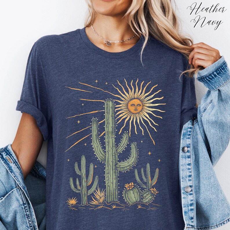 May include: Heather navy blue t-shirt featuring a desert scene with cacti and a sun with a face. The graphic includes a large central cactus, smaller cacti, and a radiant sun with a smiling face. The text "Heather Navy" is in the upper right corner.