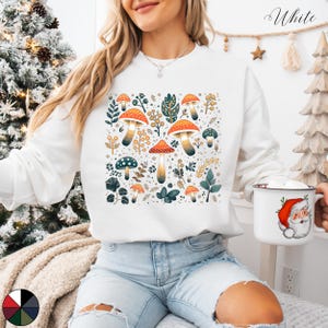 May include: White sweatshirt with a colorful mushroom and leaf pattern. The design features orange, yellow, green, and brown mushrooms with green leaves and stems.