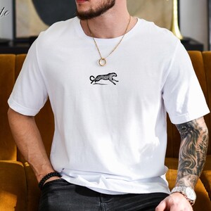 May include: White t-shirt with a black and white cheetah print design. The shirt has a crew neck and short sleeves. The word "White" is written in the top left corner of the image.