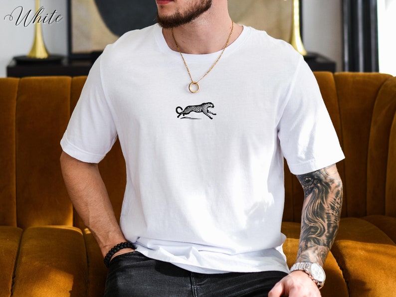 May include: White t-shirt with a black and white cheetah print design. The shirt has a crew neck and short sleeves. The word "White" is written in the top left corner of the image.