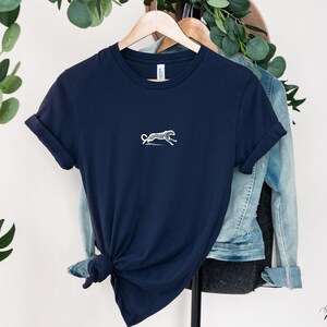 May include: A navy blue t-shirt with a white silhouette of a cheetah running on the front. The shirt is hanging on a hanger.