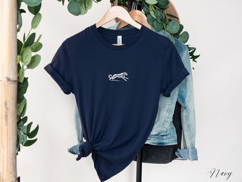 May include: A navy blue t-shirt with a white silhouette of a cheetah running on the front. The shirt is hanging on a hanger.