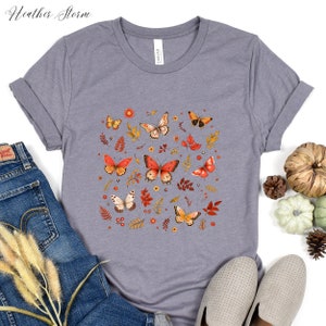 May include: A heather grey t-shirt with a print of orange and yellow butterflies, leaves, and flowers. The design is centered on the shirt.
