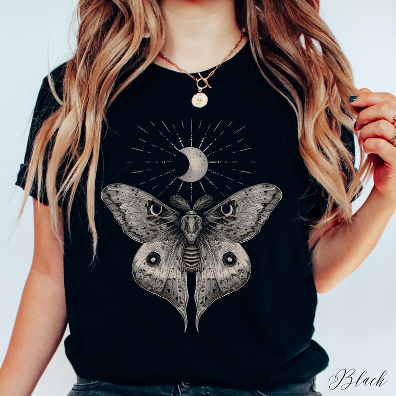 May include: Black t-shirt with a graphic of a moth with large eyes and a crescent moon with a starburst behind it.