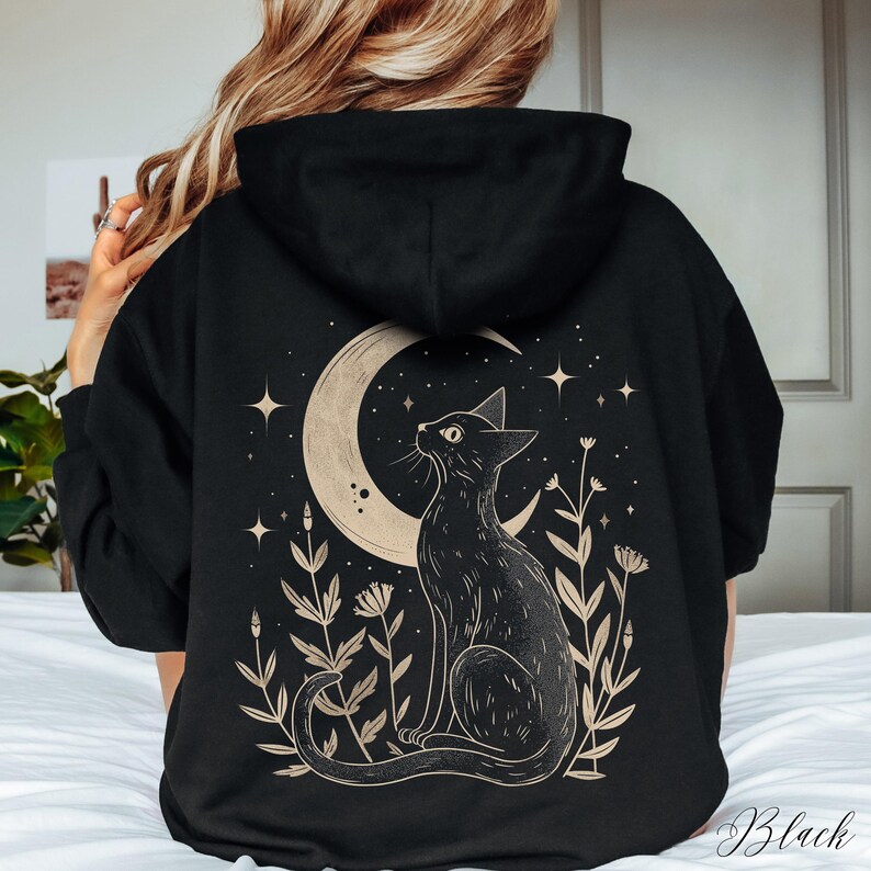 May include: Black hoodie with a graphic print of a black cat sitting under a crescent moon with stars and flowers. The text "Black" is visible in the bottom right corner of the image.