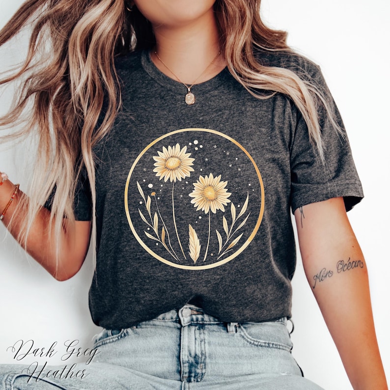 May include: Dark gray heather t-shirt featuring a gold circular design with two yellow sunflowers and foliage. The text "Dark Greg Heather" is at the bottom of the shirt.