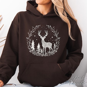 May include: Dark chocolate-colored hoodie featuring a white graphic of a deer with intricate patterns, surrounded by a wreath of branches, trees, and stars. The hoodie has a front pocket and a drawstring hood. The text "Dark Chocolate" is visible on the bottom right.