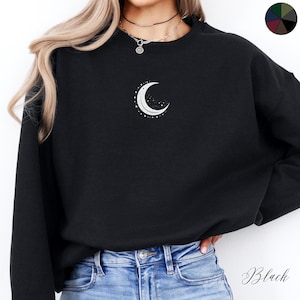 May include: Black sweatshirt with a crescent moon and stars graphic on the front. The sweatshirt has a crew neck and long sleeves.