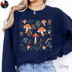 May include: Navy blue sweatshirt with a graphic of colorful mushrooms and leaves. The text "Shroom Queens" is printed on the front of the sweatshirt.