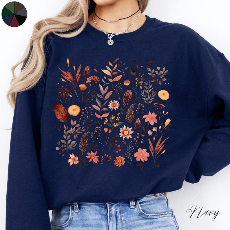 May include: A navy blue sweatshirt with a floral print featuring a variety of flowers and leaves in shades of orange, brown, and yellow. The sweatshirt has a crew neck and long sleeves.