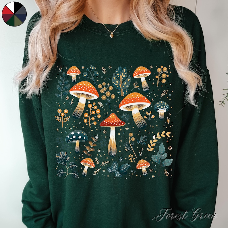 May include: Forest green sweatshirt with a colorful mushroom print. The mushrooms are red, orange, yellow, and white with brown stems. The print is surrounded by green leaves and white dots.