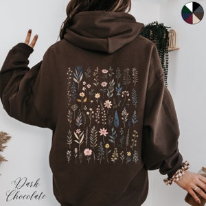 May include: A dark chocolate brown hoodie with a floral print on the back. The print features a variety of flowers and leaves in shades of pink, blue, and green.