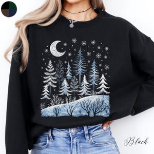 May include: Black sweatshirt with a winter forest scene featuring a crescent moon, snowflakes, and pine trees. The sweatshirt has a relaxed fit and a crew neck.