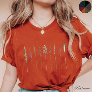 May include: A rust-coloured t-shirt with a graphic of dried flowers and grasses. The shirt has a relaxed fit and short sleeves.