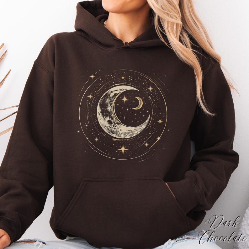 Op de afbeelding: Een donkerbruine hoodie met een gouden halve maan en sterrenontwerp. Het ontwerp is gecentreerd op de voorkant van de hoodie.