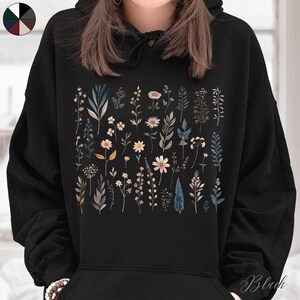 May include: Black hoodie with a floral print featuring various types of flowers and leaves in shades of blue, pink, and green.