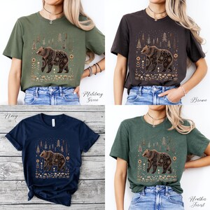 May include: Four t-shirts in military green, brown, navy, and heather forest colors. Each shirt features a detailed bear graphic with floral and tree elements. The shirts are displayed on a person.
