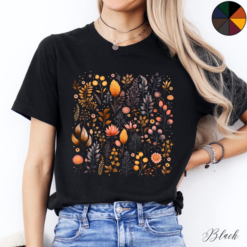 Może przedstawiać: Czarny T-shirt z nadrukiem kwiatowym przedstawiającym r&oacute;żne kwiaty i liście w odcieniach pomarańczowego, ż&oacute;łtego i r&oacute;żowego. Nadruk jest umieszczony centralnie na koszulce i pokrywa większość przodu.