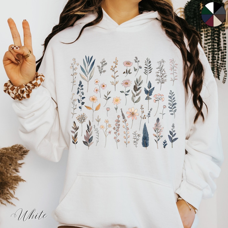 May include: White hoodie with a floral print featuring a variety of flowers and leaves in shades of pink, blue, and green.