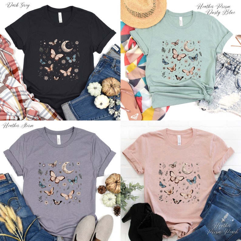 May include: Four t-shirts with a butterfly and moon graphic design. The shirts are in the colors dark gray, dusty blue, storm, and peach.