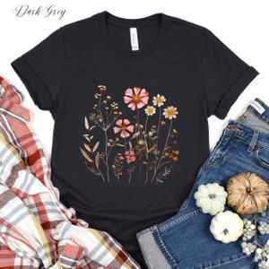May include: A dark grey t-shirt with a floral print featuring pink and brown flowers and leaves. The shirt is made of a soft, comfortable material and has a crew neck.