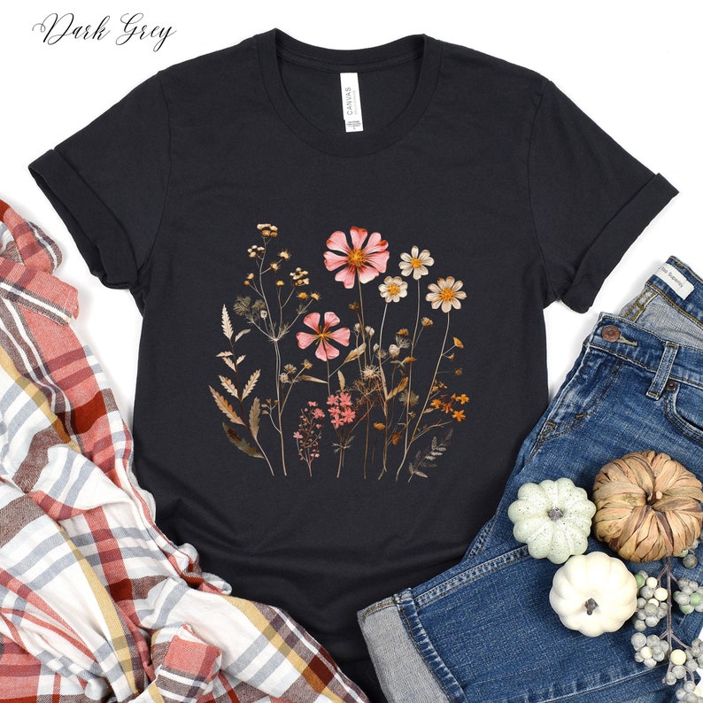 May include: A dark grey t-shirt with a floral print featuring pink and brown flowers and leaves. The shirt is made of a soft, comfortable material and has a crew neck.